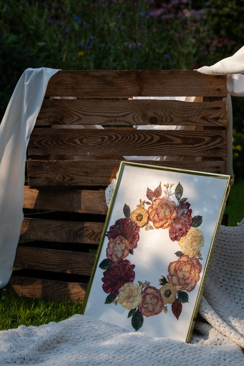 Elegancki obraz z suszonymi kwiatami w złotej ramce, kompozycja w kształcie wieńca. Idealny pamiątkowy bukiet ślubny.