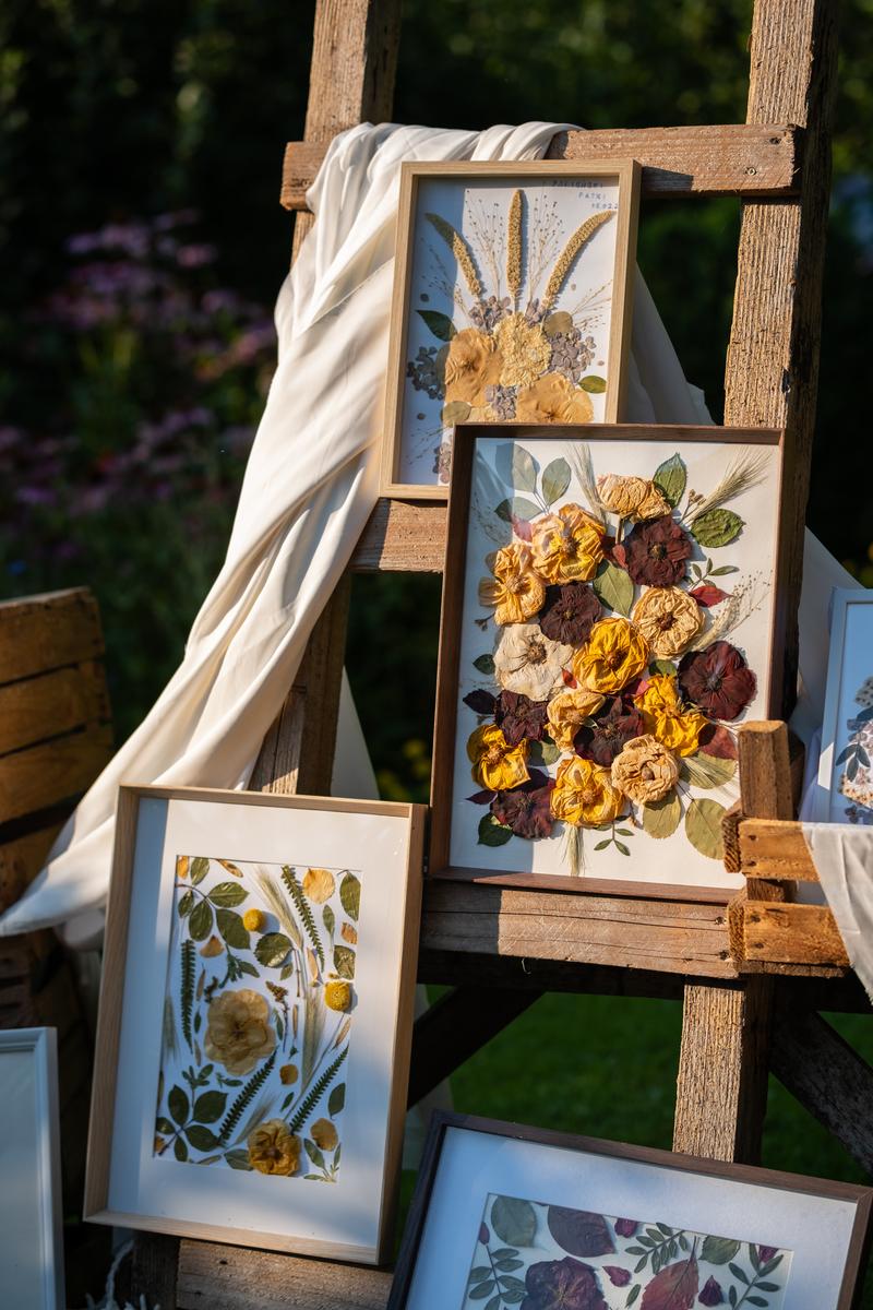 Kolekcja czterech obrazów z suszonych kwiatów Karokwiaty, prezentowana na rustykalnej drewnianej konstrukcji w ogrodzie.