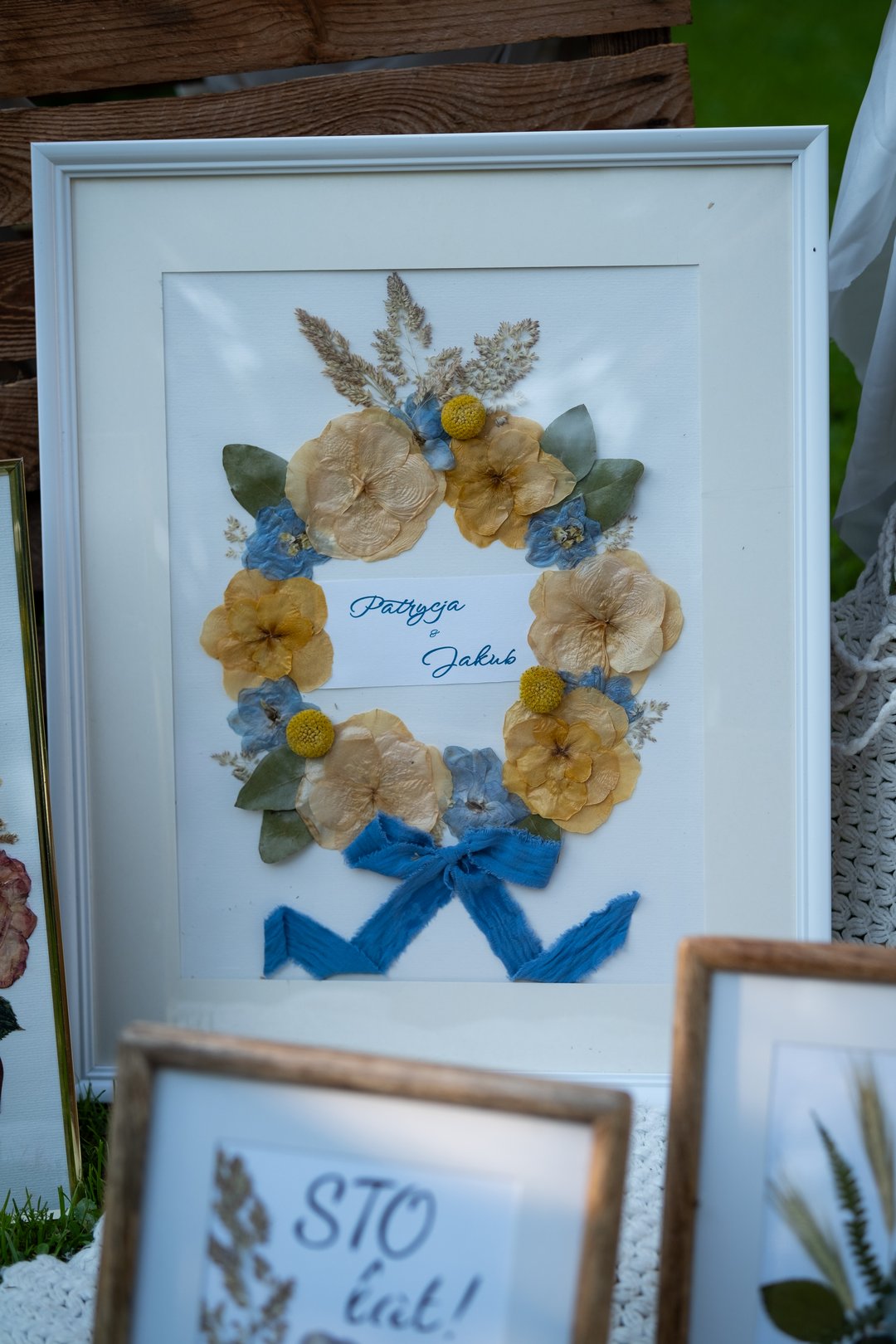 Elegancki obraz z suszonych kwiatów w białej ramce, wieniec z bukietu ślubnego Patrycji i Jakuba. Karokwiaty.