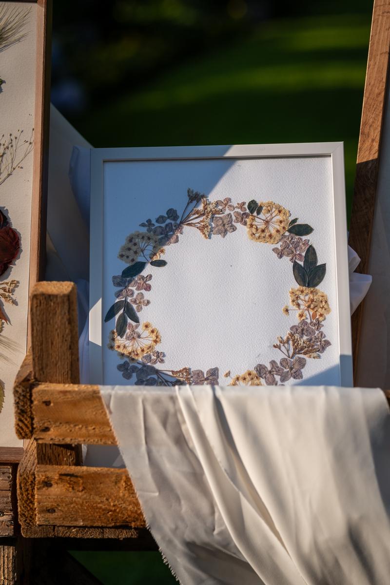 Delikatny wieniec z suszonych kwiatów w białej ramce. Elegancka kompozycja Karokwiaty w odcieniach beżu i fioletu.